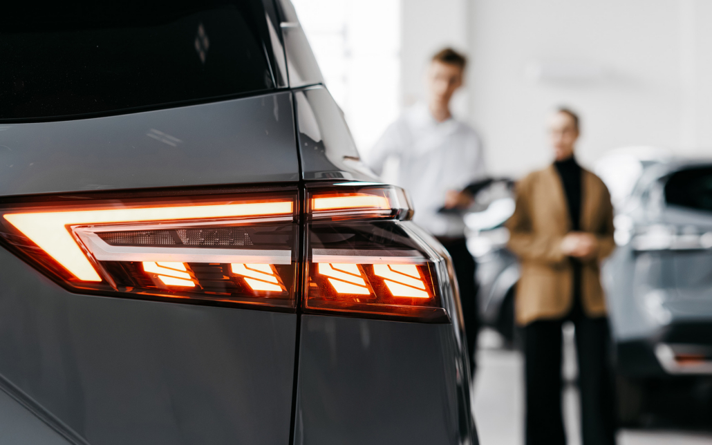 Modern Car Dealership Interior Showcasing Sleek Vehicle Rear Lights With Customers Discussing Options